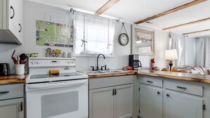A kitchen with a white stove, grey cabinets, a map on the wall, and a window with curtains. - OIBee Hive • Cute 1970s Beach Cottage 2mi to Beach (Ocean Isle Beach)
