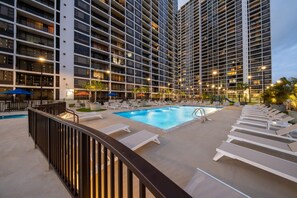 A hotel pool area with sun loungers and a swimming pool, surrounded by high-rise buildings.