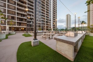 En tagterrasse med udendørs siddepladser, en stor bygning med flere altaner og en klar himmel.