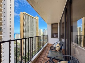 Un balcon donnant sur des immeubles de grande hauteur, une porte vitrée et une petite table avec une chaise.