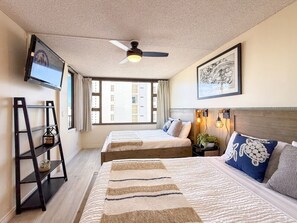 A hotel room with two beds, a ceiling fan, a TV, a framed artwork, and a window with curtains.