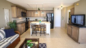 A modern kitchen with a central island, bar stools, and a TV mounted on the cabinetry.