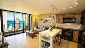 A spacious living area with a balcony, a kitchen with wooden cabinets, and a view of the ocean.