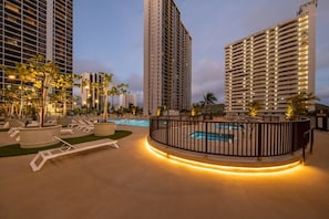 A pool area with lounge chairs, a pool, and high-rise buildings in the background. - Bright 1BR Ocean-View Retreat • Walk to Beach • Free Parking (Honolulu)