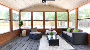 Eine überdachte Terrasse mit Korbmöbeln, einem Tisch mit Gläsern und einer Pflanze.