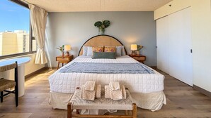 Un dormitorio con una cama grande, mesitas de noche, una pequeña mesa con sillas y vistas a edificios.