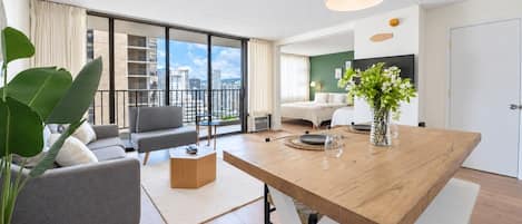 A modern living room with a wooden dining table, grey sofa, and a large window with a city view.