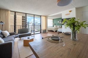 A modern living room with a sofa, coffee table, and a dining table with a vase of flowers. - Fresh 1 Bedroom with Parking at Waikiki Banyan !! (Honolulu)