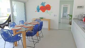A dining area with a glass table, blue chairs, and a wall mural.