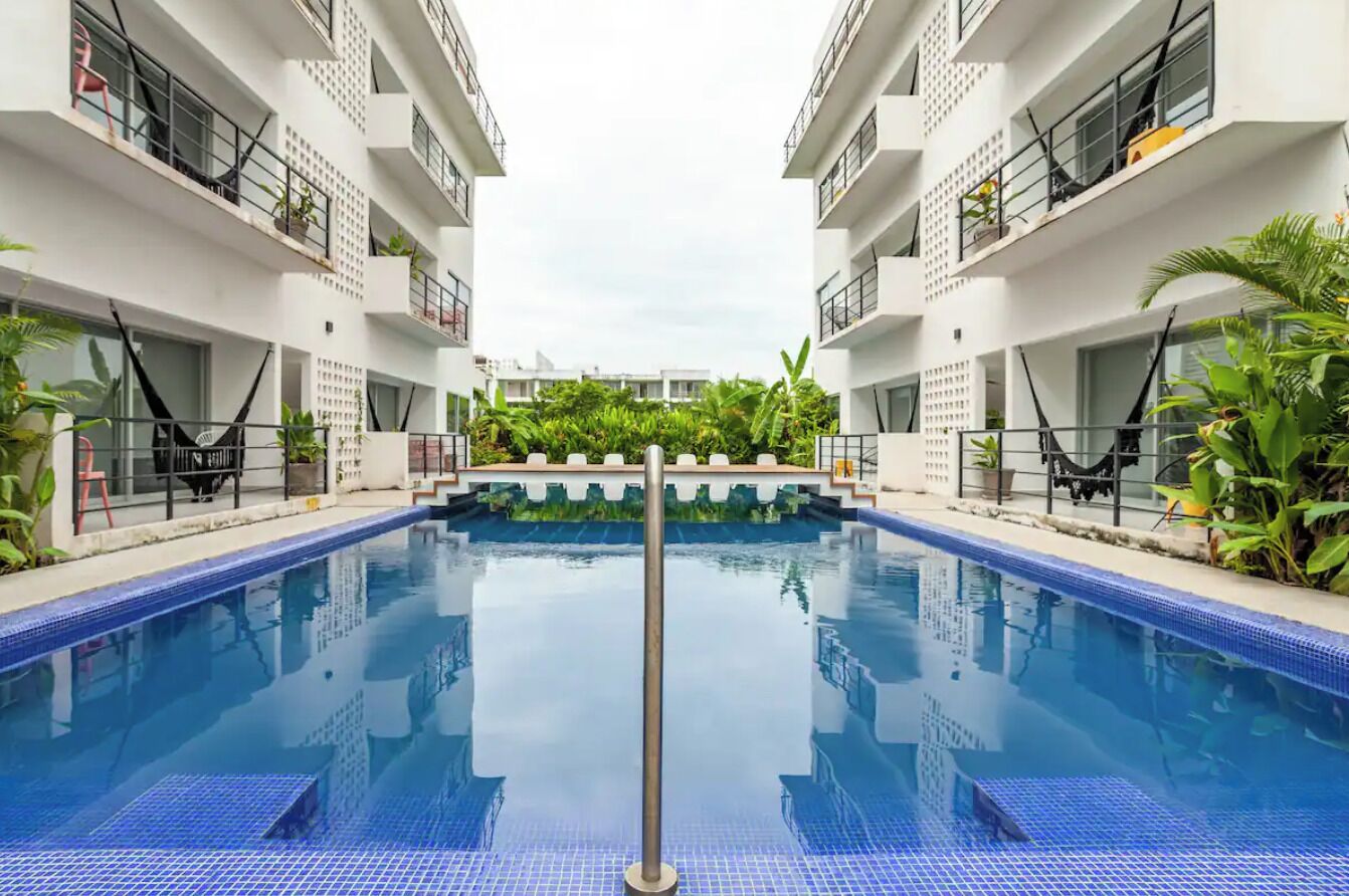 Un hotel moderno con piscina central, balcones con plantas y cielo despejado.
