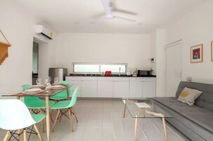 Una cocina moderna con armarios blancos, un comedor con sillas verdes y un sofá gris.