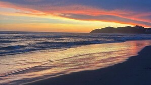Een strand met een zonsondergang, golven en een berg in de verte.