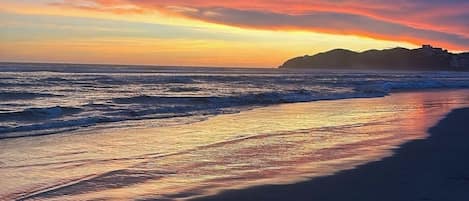 Una playa con un atardecer, olas y una montaña distante.