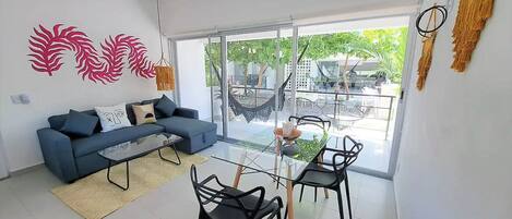 A modern living room with a sofa, coffee table, and chairs, a large sliding glass door to a balcony with outdoor furniture.