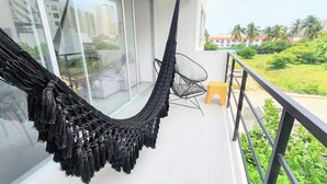 Een balkon met een zwarte hangmat, een klein geel krukje en een stoel.