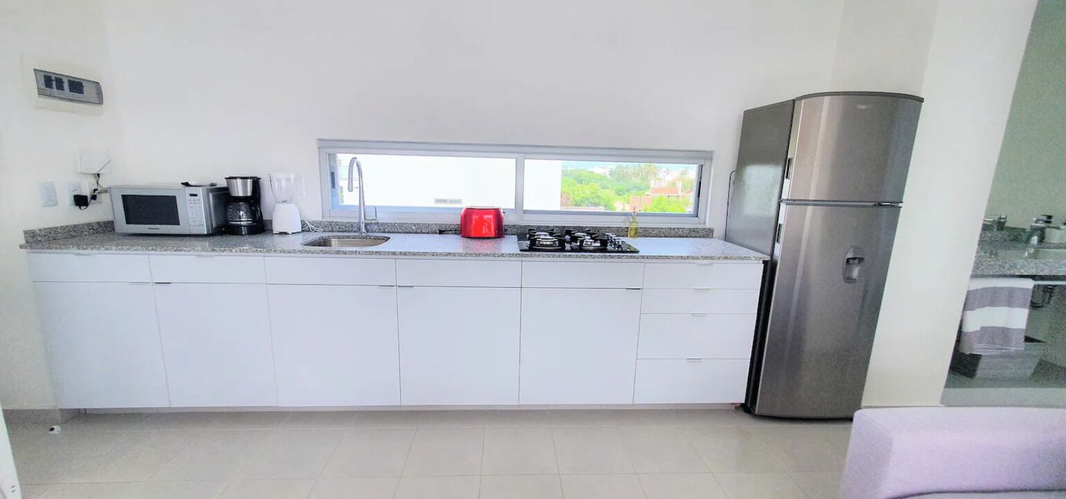 Eine moderne Küche mit weißen Schränken, einem Edelstahlkühlschrank, einer Mikrowelle, einem roten Toaster und einem Fenster für natürliches Licht.