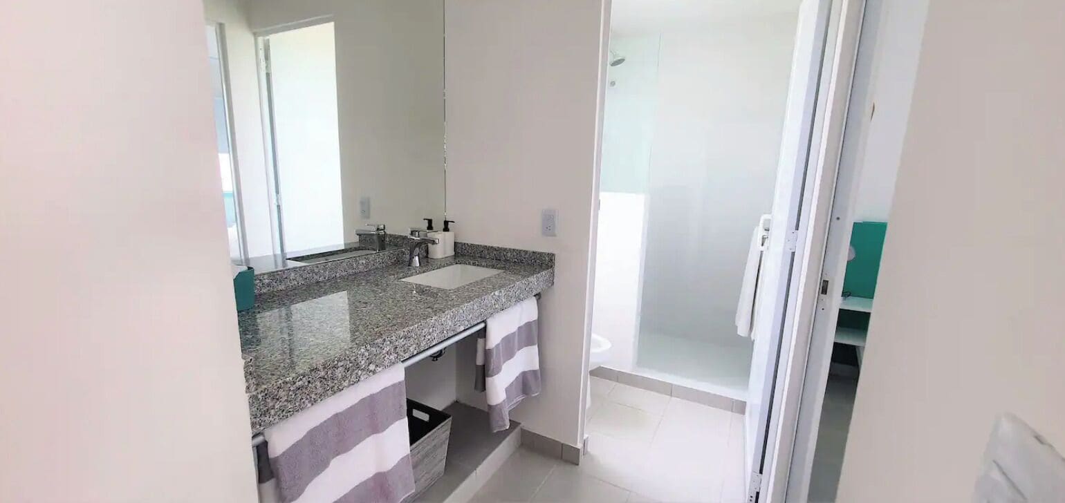 Een badkamer met een granieten aanrecht, een spiegel, een douche en een handdoekhouder.