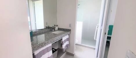 A bathroom with a granite countertop, a mirror, a shower, and a towel rack.