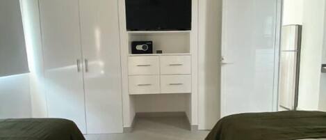 Un dormitorio con dos camas, un televisor en un estante y un armario.