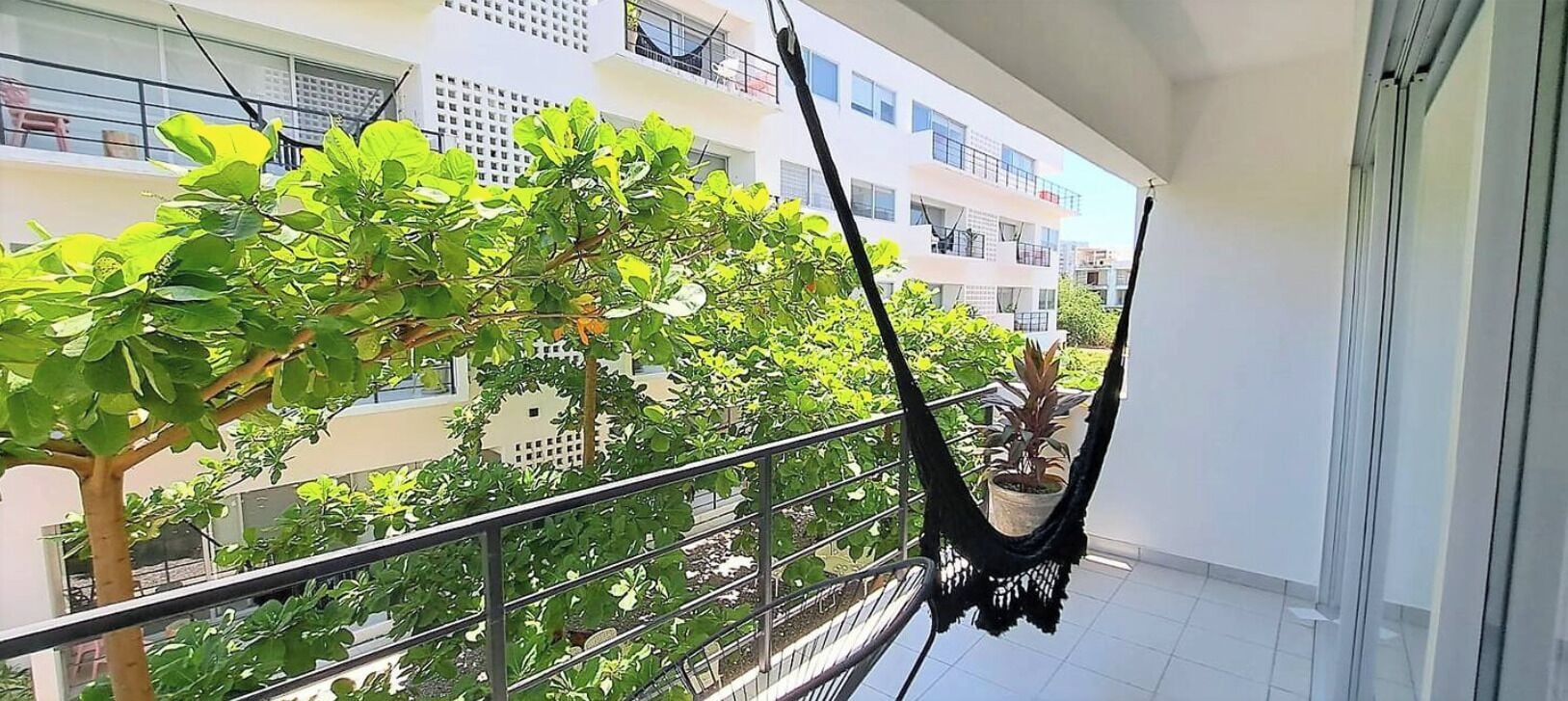 A balcony with a hammock, potted plants, and a view of surrounding buildings.