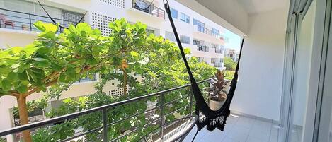 A balcony with a hammock, potted plants, and a view of surrounding buildings.
