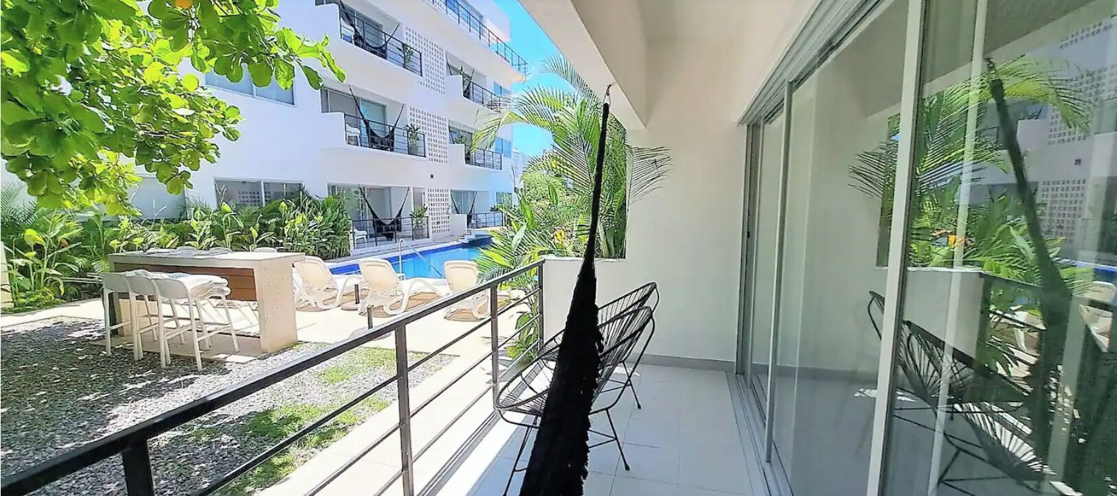 Varanda com piscina, cadeiras brancas e porta de vidro.