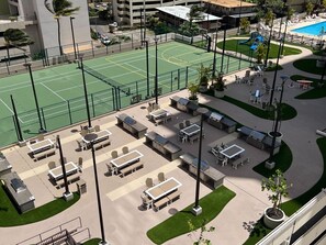 Un court de tennis extérieur avec des siÚges et un espace piscine.