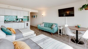 A modern living room with a sofa, a teal couch, and a dining area with a table and chairs.