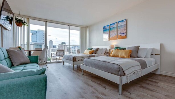 A modern hotel room with two beds, a balcony, and a city view.