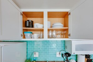 A kitchen with two open cabinets containing dishes and glasses. - High Floor Waikiki Studio w/ Free Parking | Walk to Beach (Honolulu)