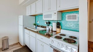 A compact kitchen with white cabinets, a microwave, a stove, and a trash bin.