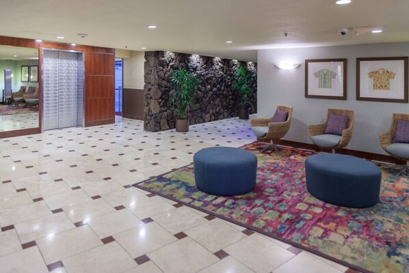 A lobby with a tiled floor, a stone wall with plants, wicker chairs, and a colorful rug. - High Floor Waikiki Studio w/ Free Parking | Walk to Beach (Honolulu)