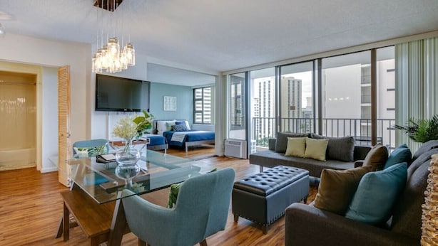 Una sala moderna con una mesa de comedor de vidrio, un sofá y un balcón con vistas a la ciudad.