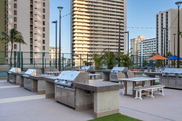 Outdoor barbecue stations, tables, and chairs in an urban setting with tall buildings in the background.