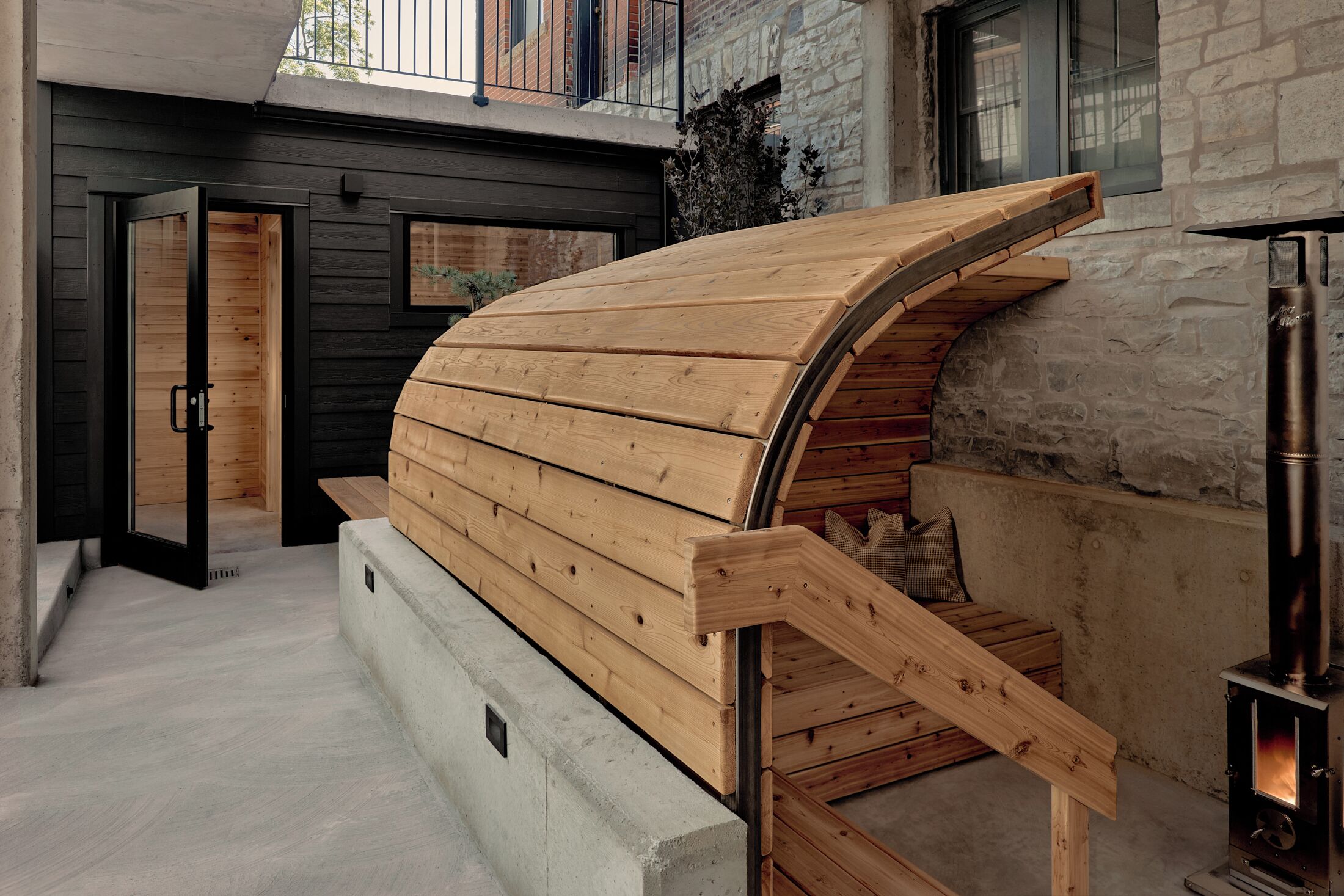 A modern outdoor seating area with a curved wooden bench and a stone fireplace.