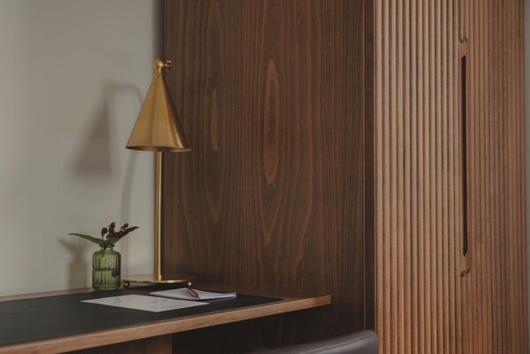 Un bureau en bois, une lampe, un vase avec des fleurs et des papiers.