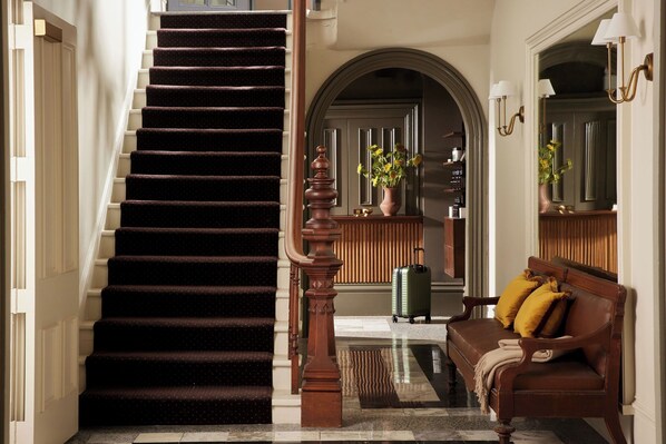 Un escalier recouvert d’une moquette sombre, une rampe en bois et un canapé en cuir marron agrémenté de coussins jaunes.