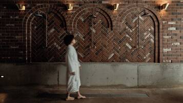 A person walking past a brick wall with arched openings and wall-mounted lights.