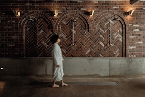 A person walking past a brick wall with arched openings and wall-mounted lights.
