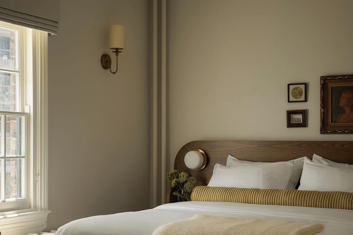 Un lit bien fait, agrémenté d’une couverture blanche moelleuse, d’une tête de lit en bois et de deux tableaux encadrés accrochés au mur.