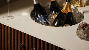 Un coin bar doté d’un comptoir blanc, d’un robinet doré et de bouteilles de champagne maintenues au frais dans de la glace.