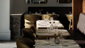 Uma área de refeições com uma mesa posta para dois, um espelho sobre a mesa e arandelas com espelhos redondos.