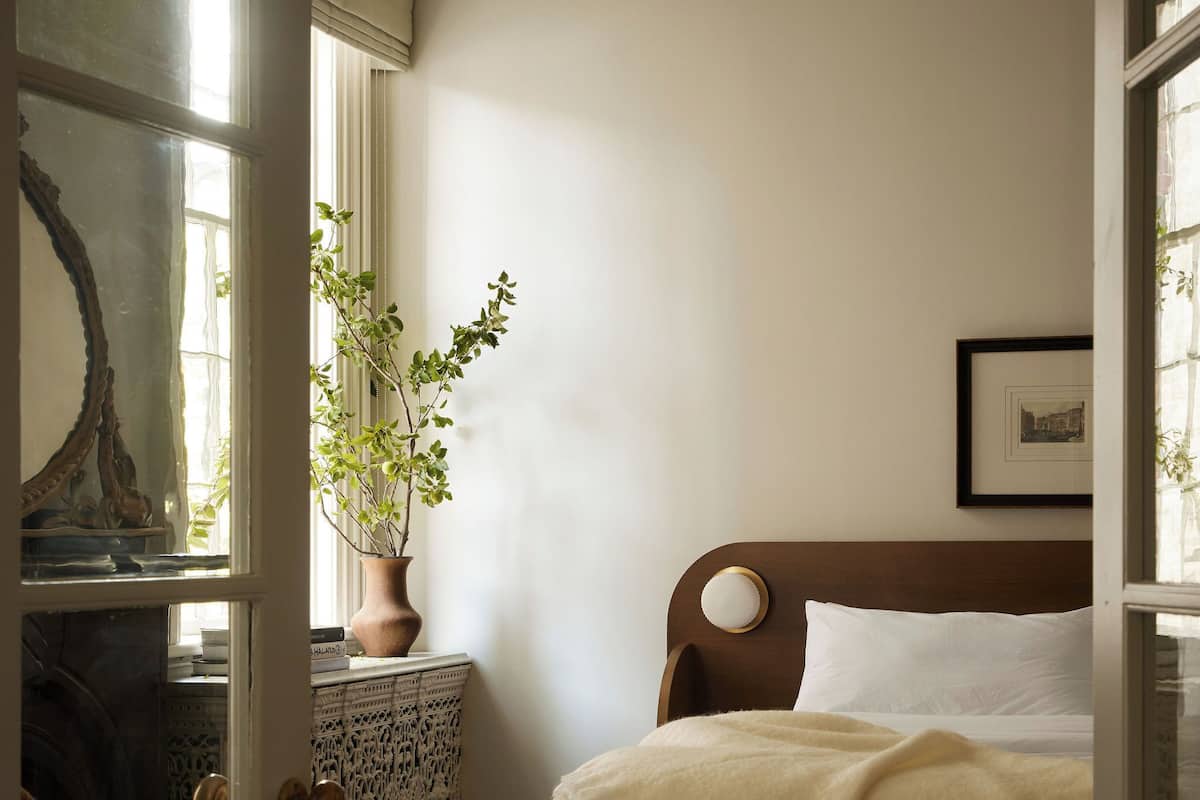 Une chambre à coucher avec un lit en bois, une plante en pot, un miroir et un tableau encadré accroché au mur.