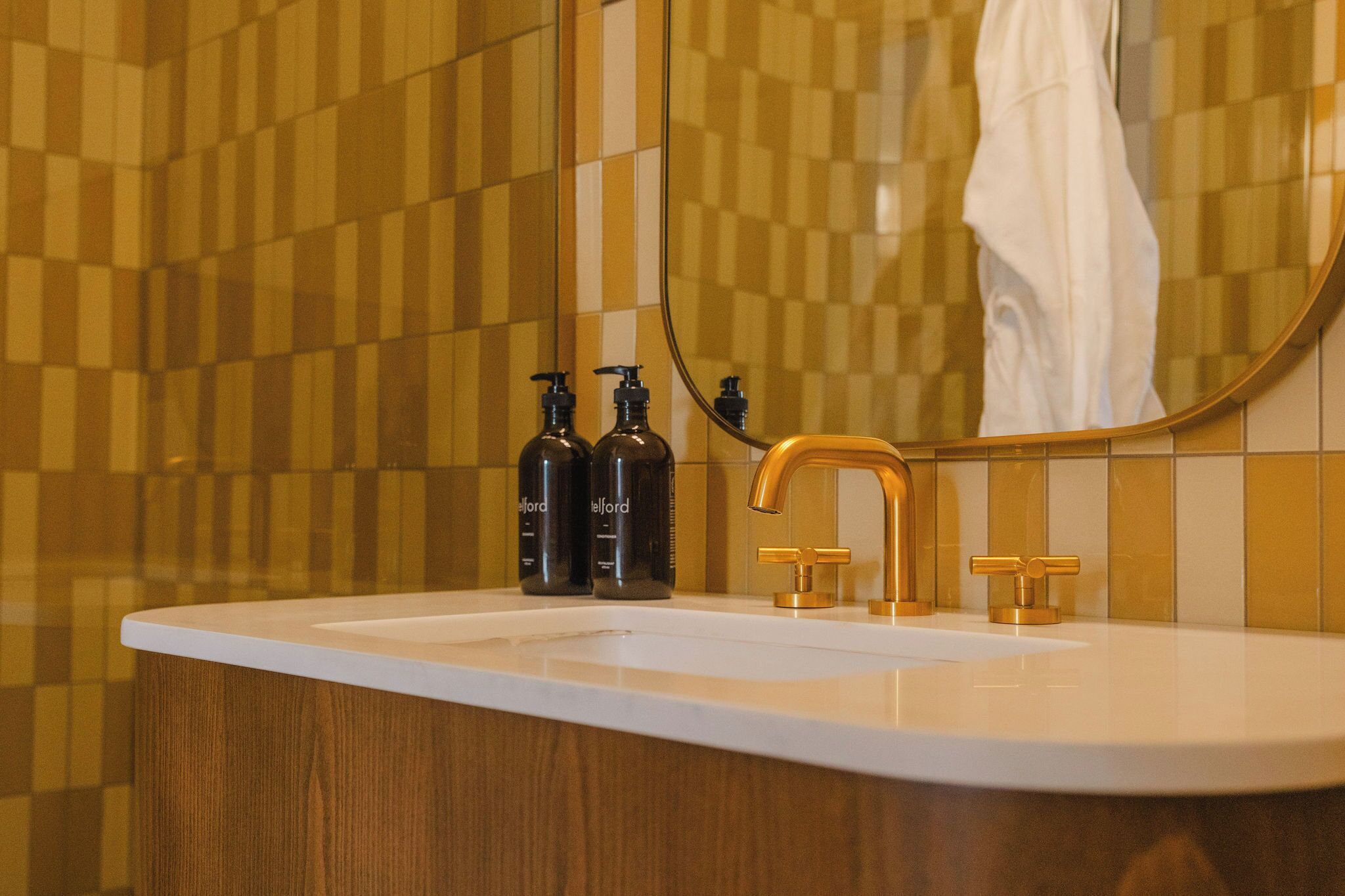 Ein Badezimmer mit einem weißen Waschbecken, goldenen Wasserhähnen und zwei schwarzen Flaschen auf der Ablagefläche.