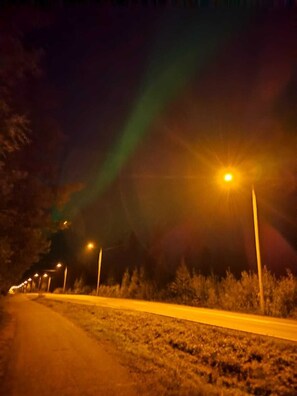 A road at night with streetlights and a visible aurora. - LT Villa (Rovaniemi)
