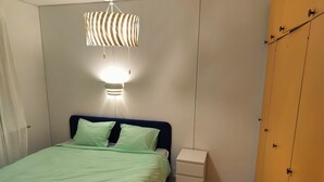 A bedroom with a bed, a bedside table, a wardrobe, and a hanging light fixture. - LT Villa (Rovaniemi)