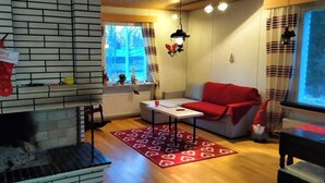 A cozy living room with a fireplace, a red sofa, and a patterned rug. - LT Villa (Rovaniemi)