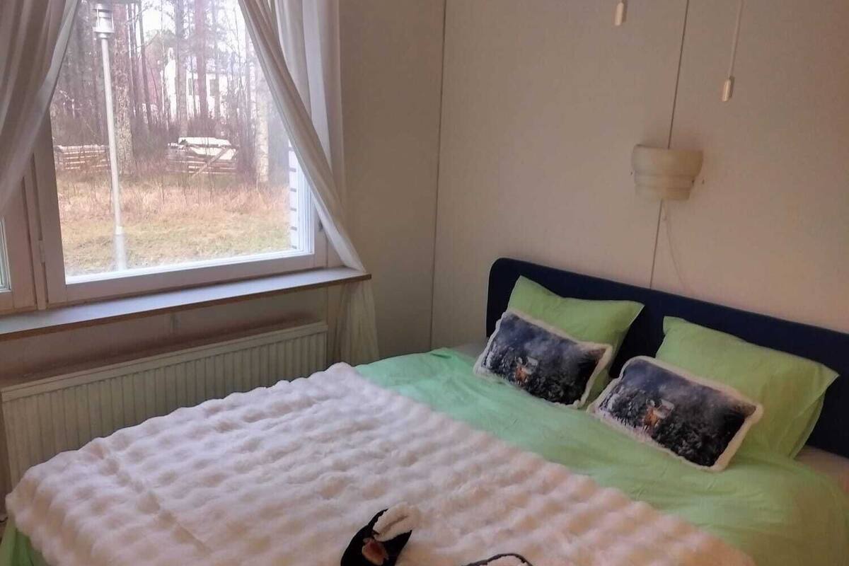 A bedroom with a bed, a window with curtains, a hanging light fixture, and a radiator.