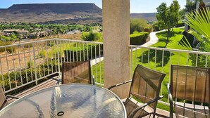 Ein Balkon mit Glastisch und Stühlen, der auf einen angelegten Garten und ferne Berge blickt.