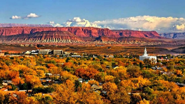 A town with autumn foliage, a prominent white church, and a flat landscape with distant red rock formations.